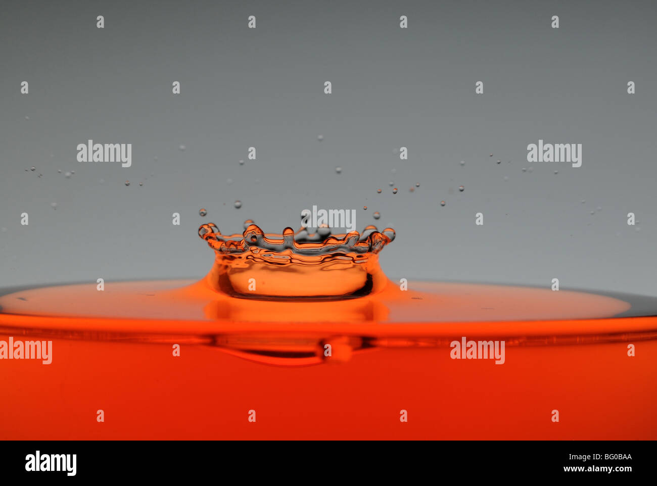 Une goutte d'eau orange formant une couronne comme il éclabousse dans un verre rempli de liquide, rétro-éclairé pour le contraste. Banque D'Images