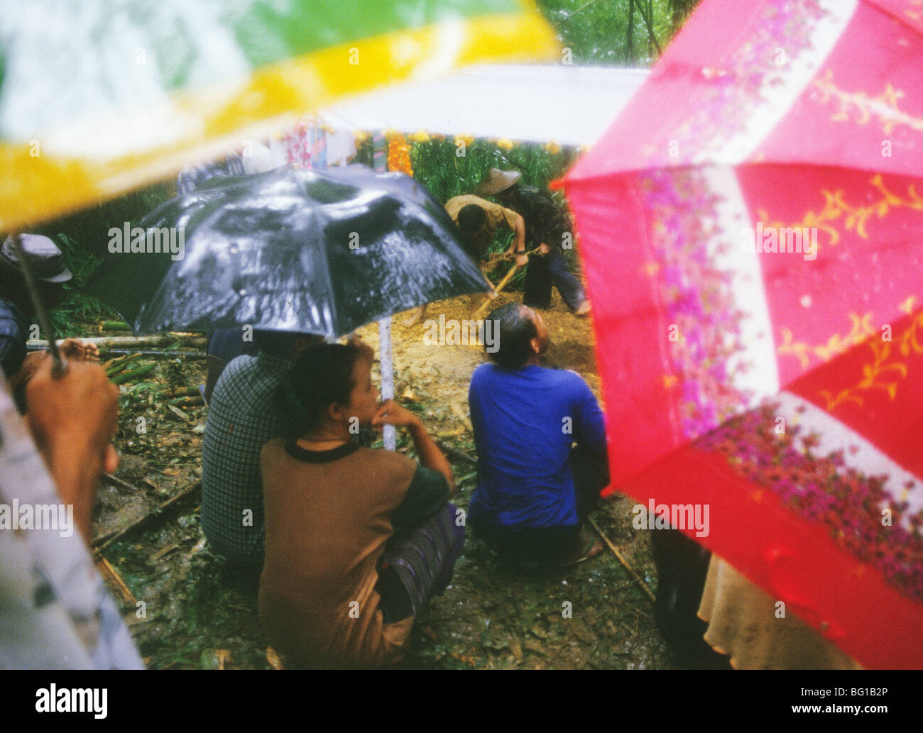 Dans une forte pluie dans la jungle le long de la Thaïlande/Birmanie Myanmar(Maintenant) frontière près de Mae Hong Son en Thaïlande avec des personnes à la recherche de parasols, fossoyeurs creusent une tombe pour un réfugié birman de 24 ans homme qui a été tué en sautant sur une mine terrestre. Banque D'Images