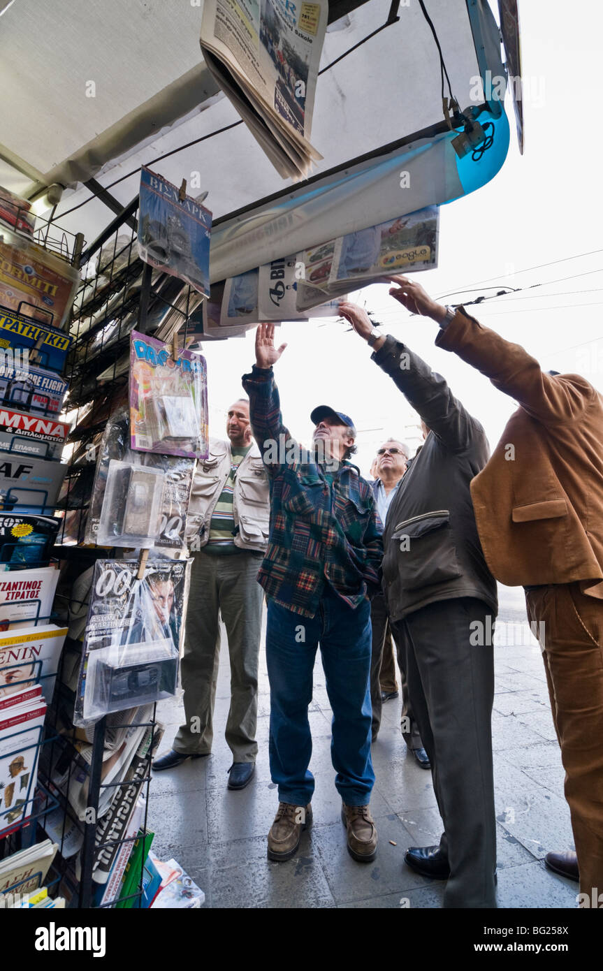 Lire les gros titres sur les journaux affichés ci-dessus un periptero (news) kiosque de la Place Omonia, dans le centre d'Athènes, Grèce. Banque D'Images