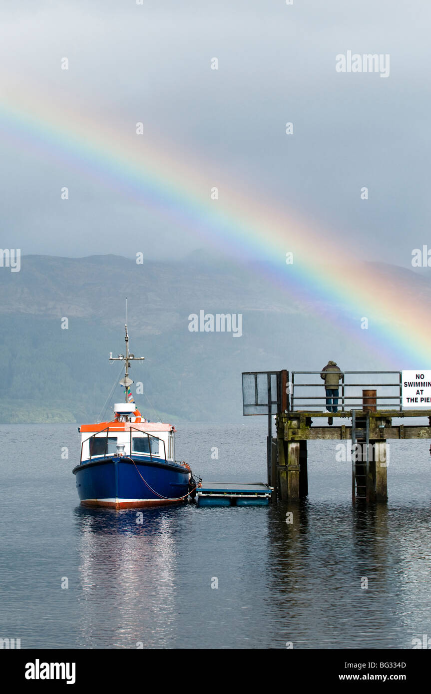 Petit bleu bateau amarré au quai de Luss sur le Loch Lomond avec rainbow en arrière-plan Banque D'Images