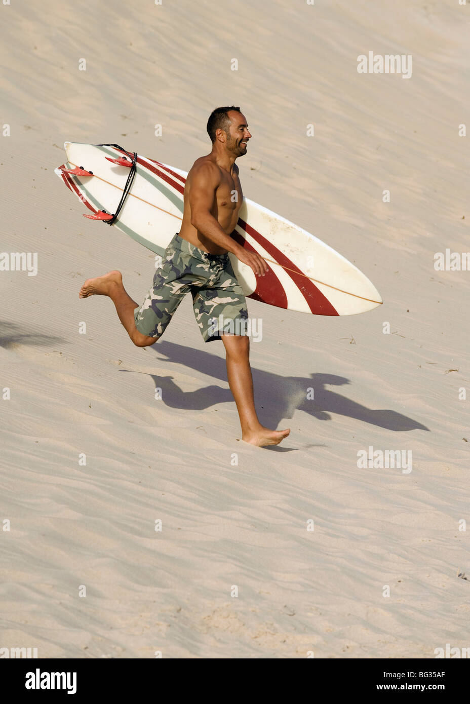 Homme qui court avec un surf sur la plage Banque D'Images