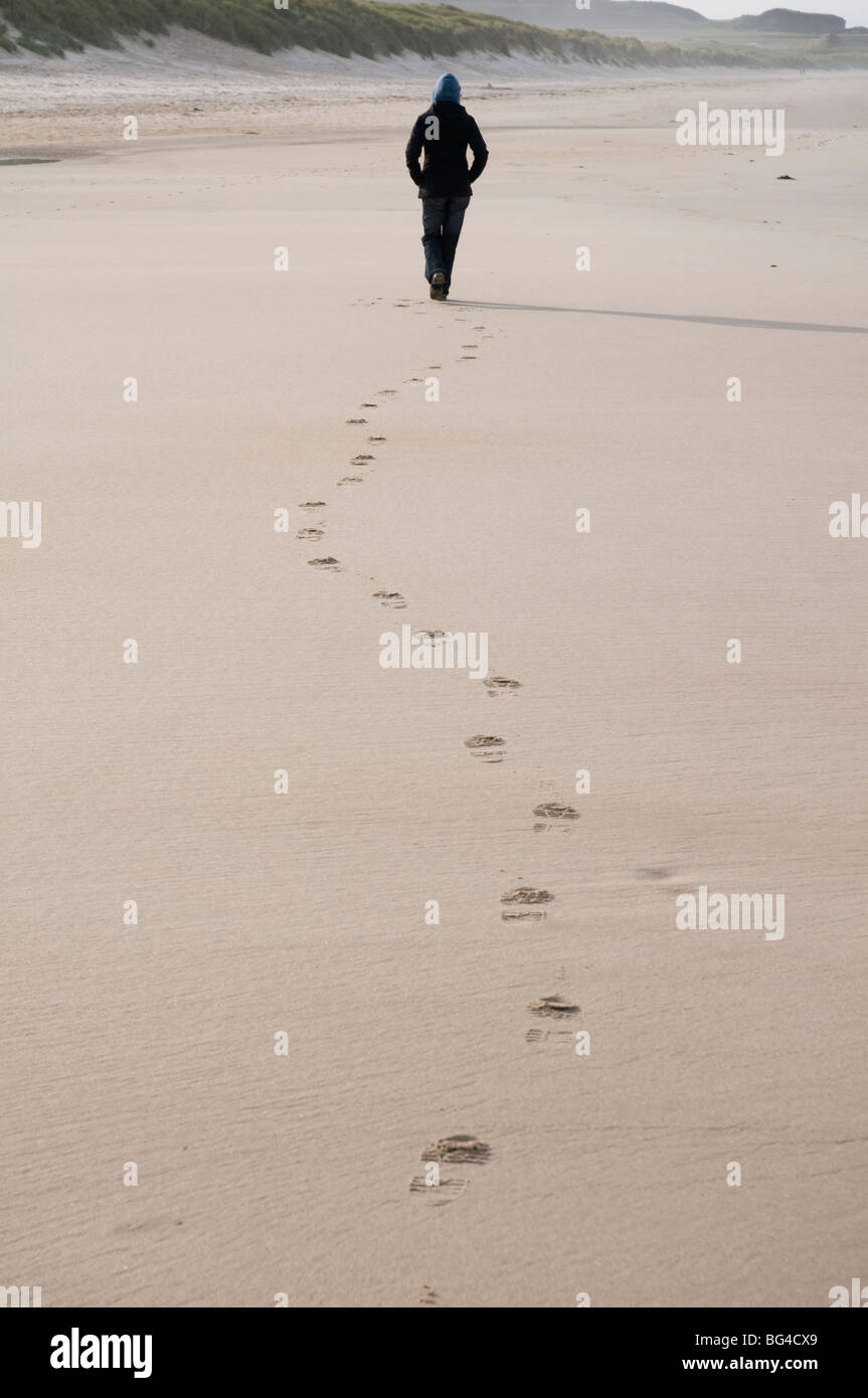 Une figure solitaire laisse des empreintes de pas sur la plage de sable en Northumbrie Bamburgh England UK Banque D'Images