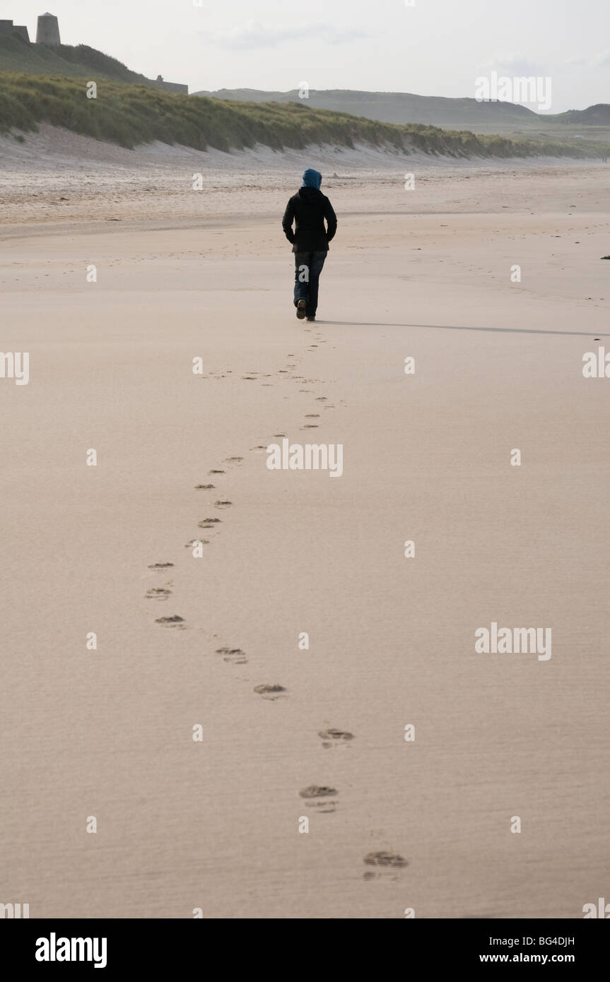 Une figure solitaire laisse des empreintes de pas sur la plage de sable en Northumbrie Bamburgh England UK Banque D'Images