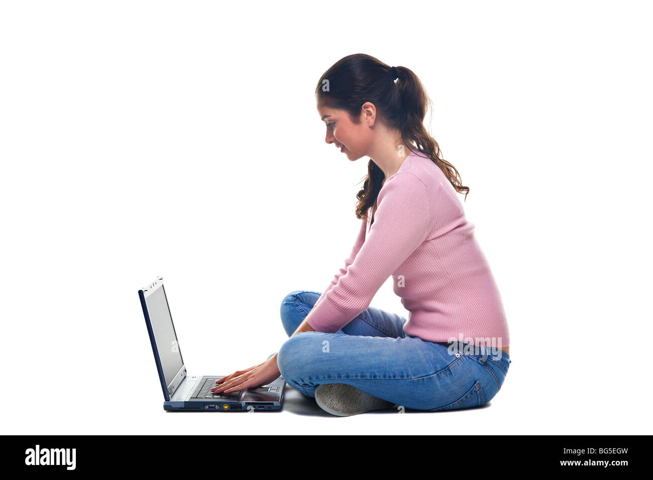 Young woman in casual clothing assis sur un sol blanc en utilisant un ordinateur portable, fond blanc. Banque D'Images