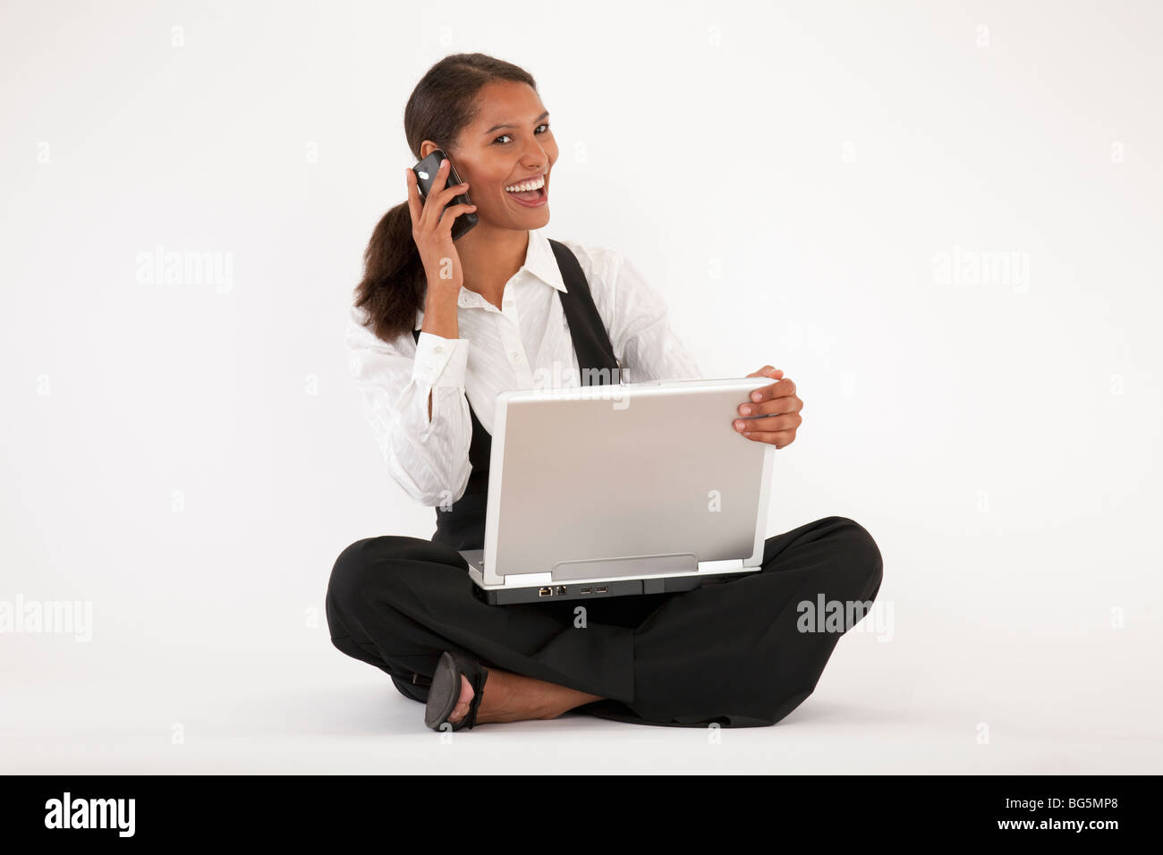Jeune femme assise sur le sol à l'aide d'ordinateur portable et téléphone cellulaire. Format horizontal. Banque D'Images