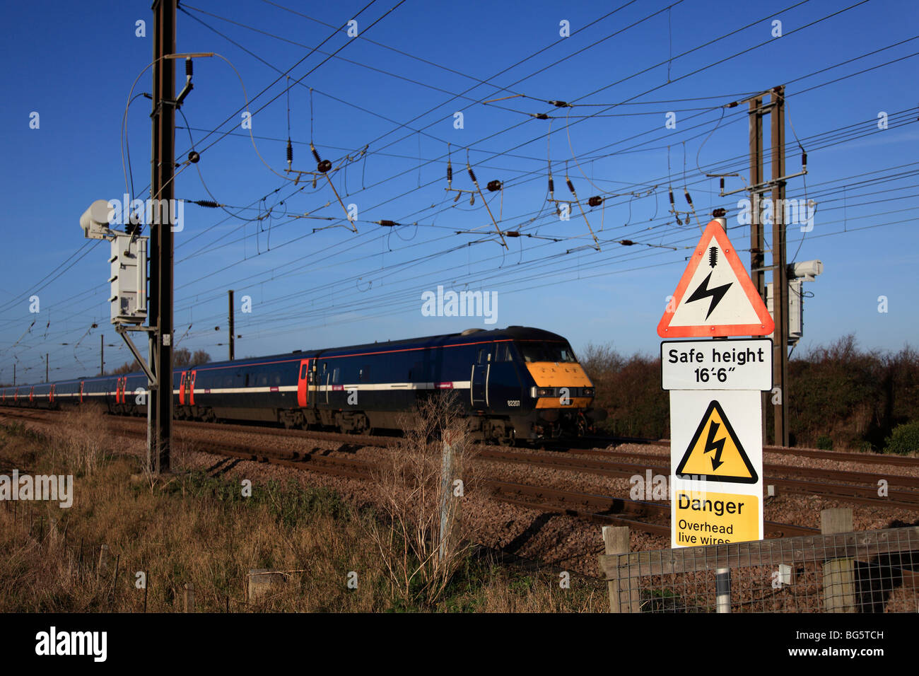 82207 Train Accélération Passage fils sous le signe de danger dans les passage barrière ligne côtière Est Peterborough Banque D'Images