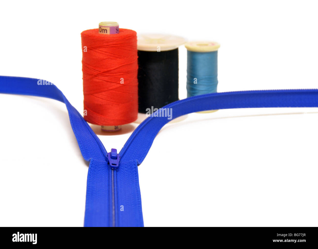 Une découpe d'un zip bleu avec des bobines de rouge, noir et bleu du fil à coudre. Banque D'Images