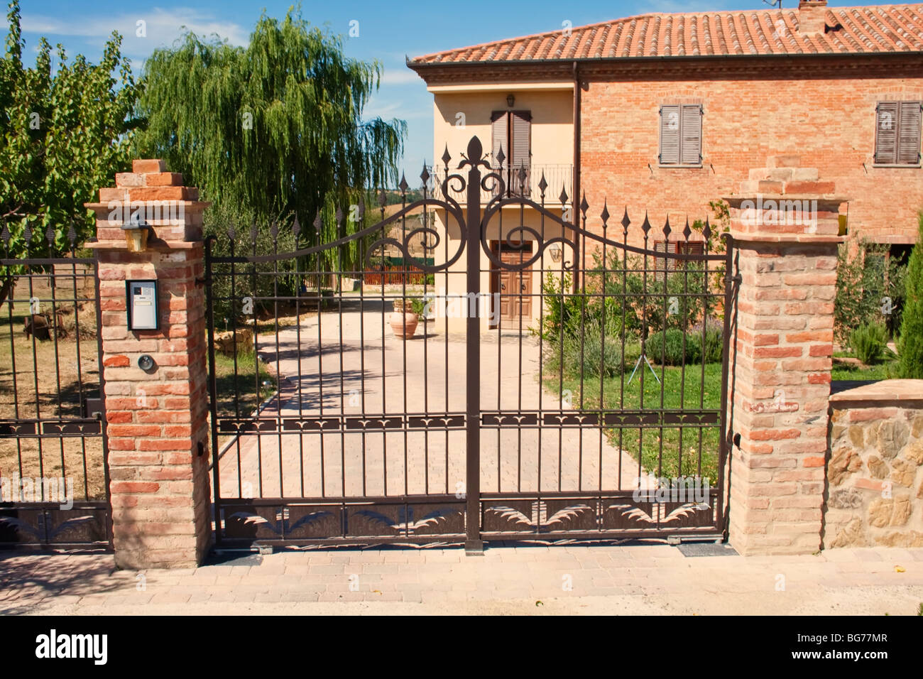 Élégante porte en fer forgé menant à une maison traditionnelle en brique avec une végétation luxuriante. Banque D'Images