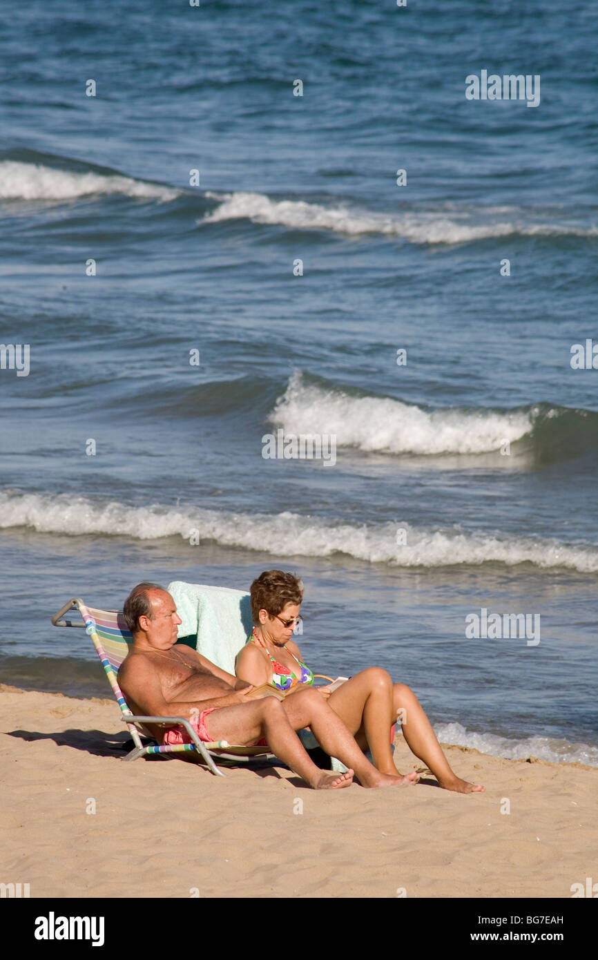 AVANT LES TÉLÉPHONES PORTABLES, 2007 : un couple plus âgé lisant un livre et bronzant plage à la station balnéaire touristique de Sitges près de Barcelone Espagne Banque D'Images