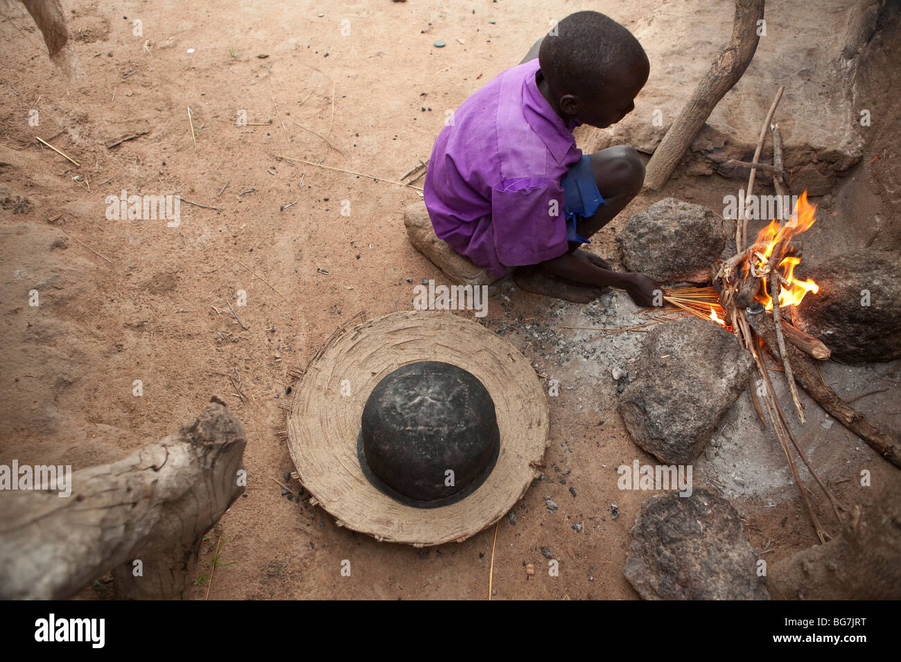 Un garçon de cuisiniers au-dessus d'un feu de camp de réfugiés en Acowa Amuria, District de l'Ouganda, l'Afrique de l'Est. Banque D'Images