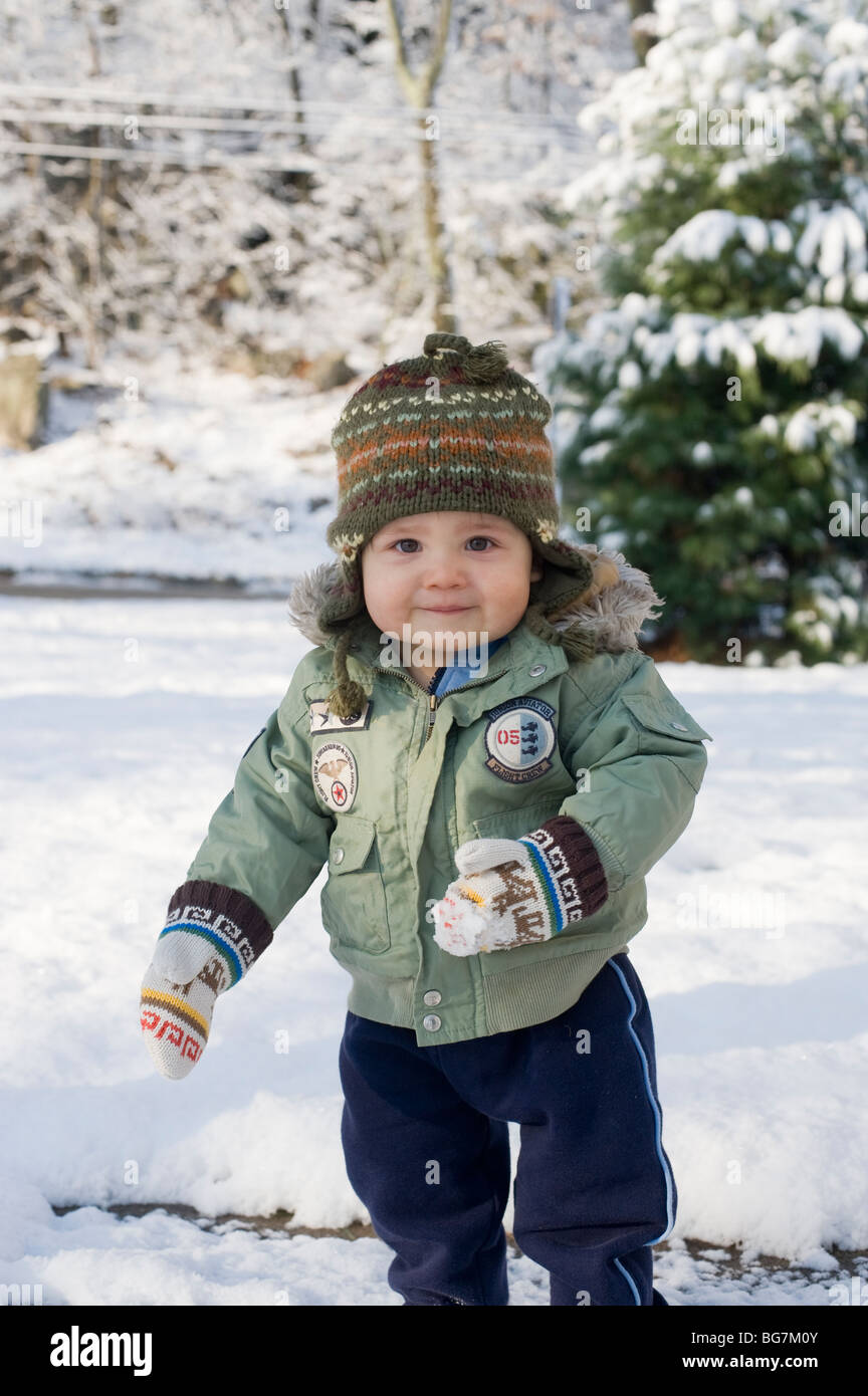 11 mois garçon hispanique joue dans la neige fraîchement tombée dans sa cour d'avec sa mère. Modèle droit est libéré. Banque D'Images