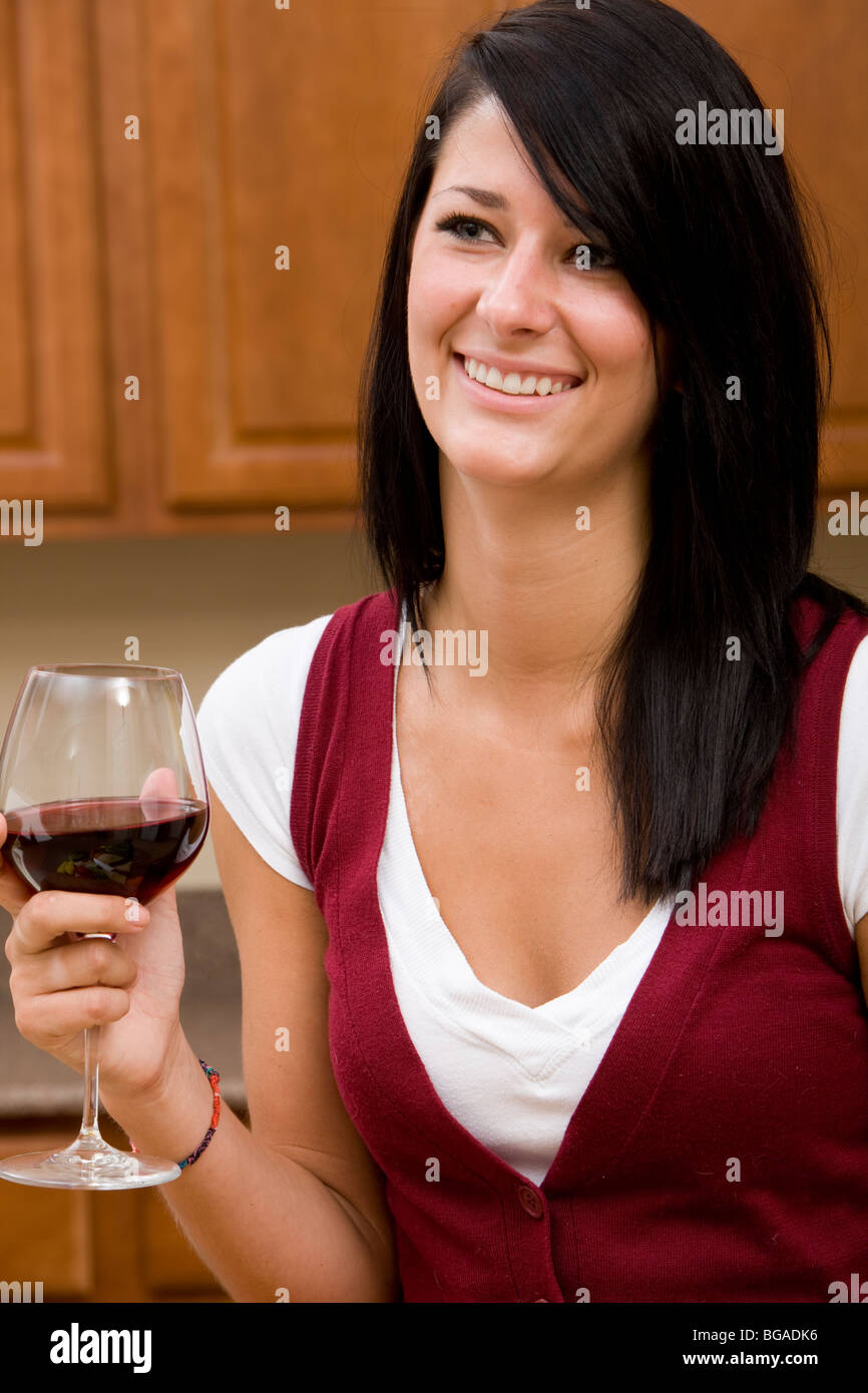 Une jeune femme bénéficie d'un verre de vin rouge à la maison dans sa cuisine. Banque D'Images