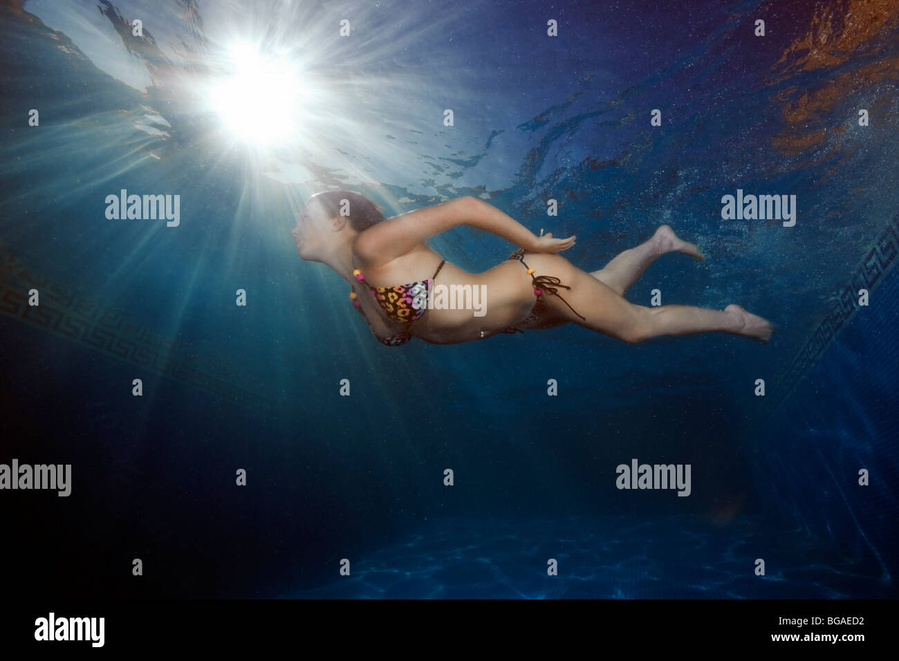 Un sunburst sur une surface gris forme l'backdop d'une jeune fille portant un bikini blanc nageant à travers les rayons de sous-marine. Banque D'Images