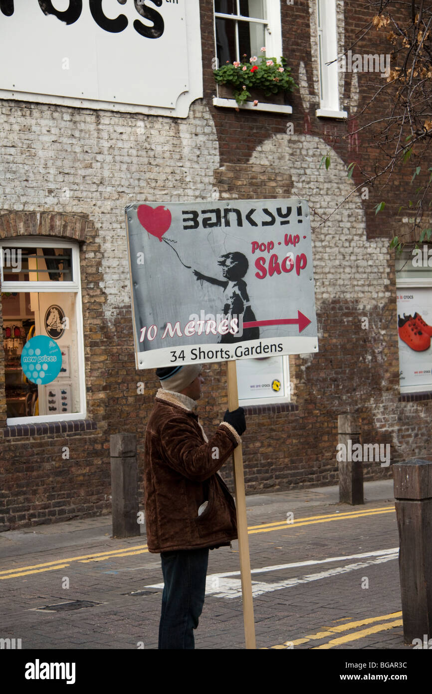 Homme tenant un Banksy pop up shop sign, Covent Garden, London, England, UK Banque D'Images