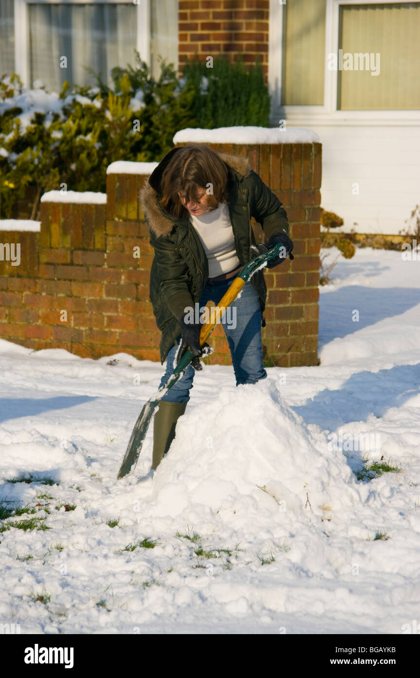 Femme personne Clearing déblayer la neige avec une pelle pelle en dehors de sa maison Banque D'Images