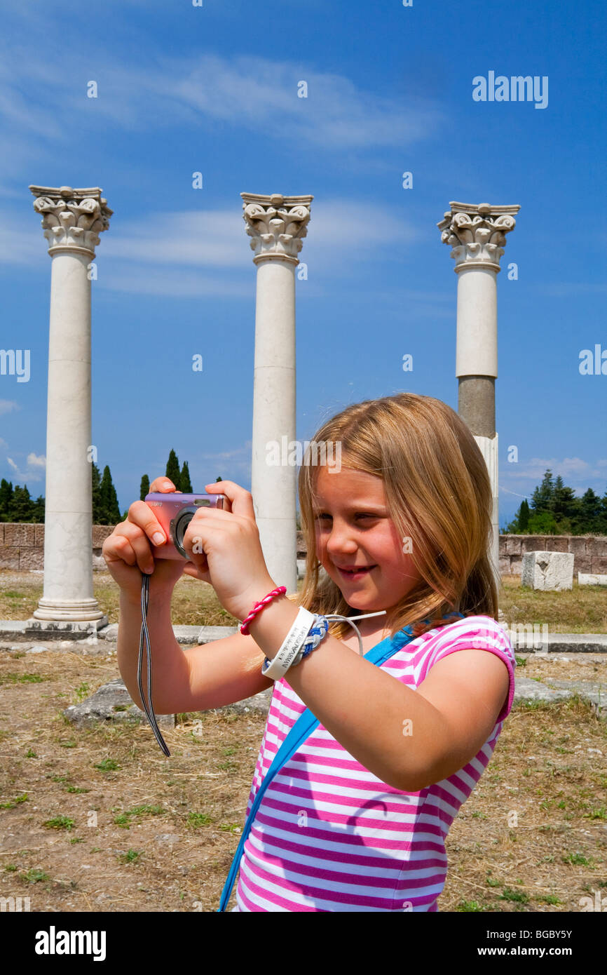 Fillette de huit ans à l'aide d'un appareil photo numérique pour prendre une photo de ruines antiques sur l'île grecque de Kos avec colonnes derrière Banque D'Images