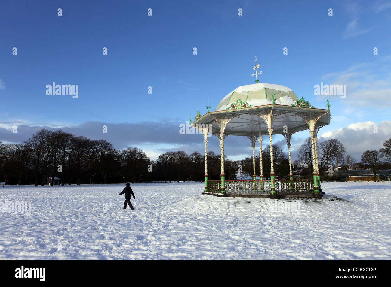 Walker en avant du kiosque traditionnel victorien dans Duthie Park à Aberdeen, Écosse, Royaume-Uni, vu dans la neige en hiver Banque D'Images