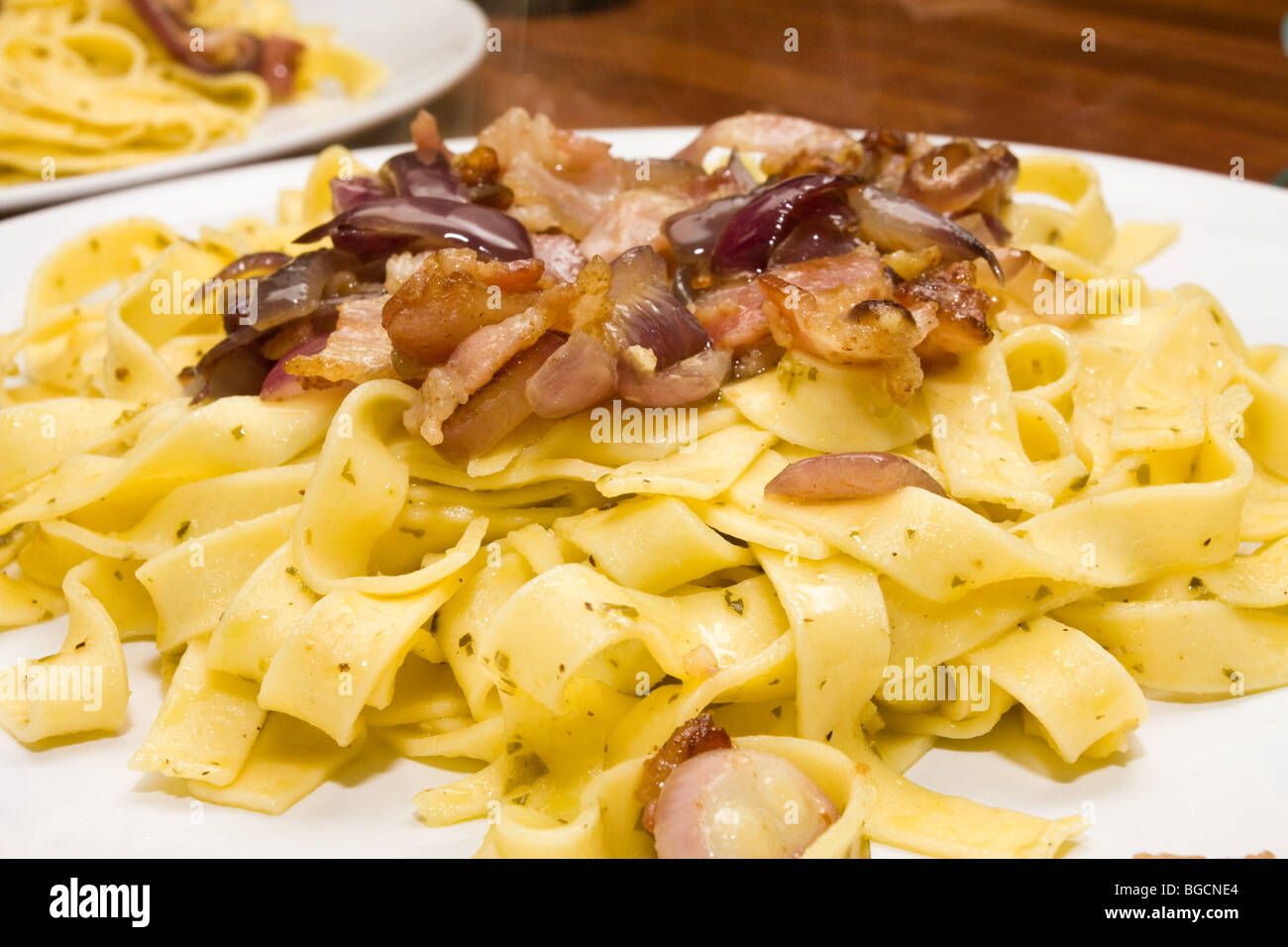 Assiette de tagliatelles sautées dans l'huile d'olive et au pesto avec lard grillé et oignon rouge. Banque D'Images