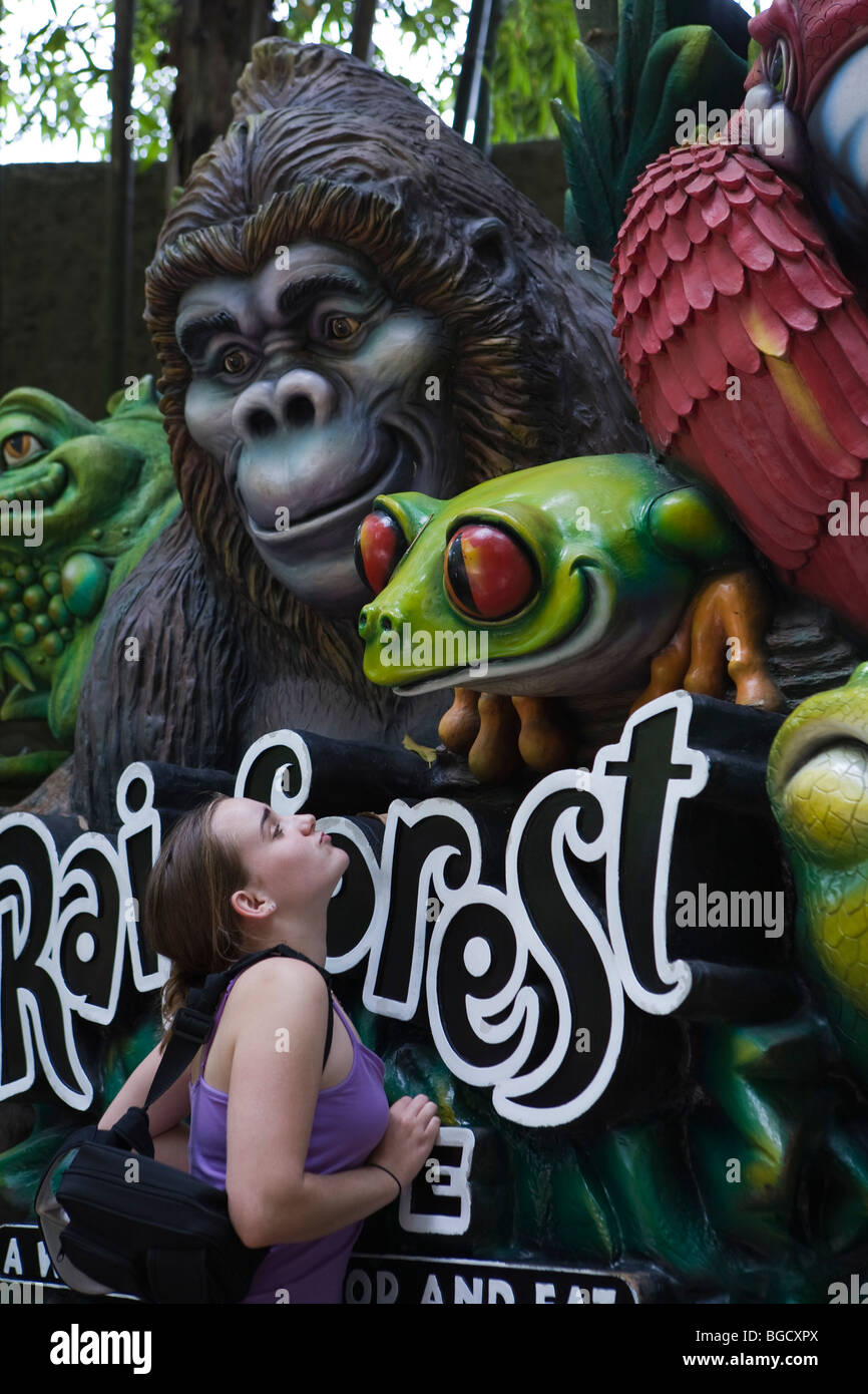 Drôle et mignon adolescente atteignant jusqu'à embrasser la grenouille verte géant souriant un gorille géant sourit en regardant une smifrom Rainforest Cafe sign Banque D'Images