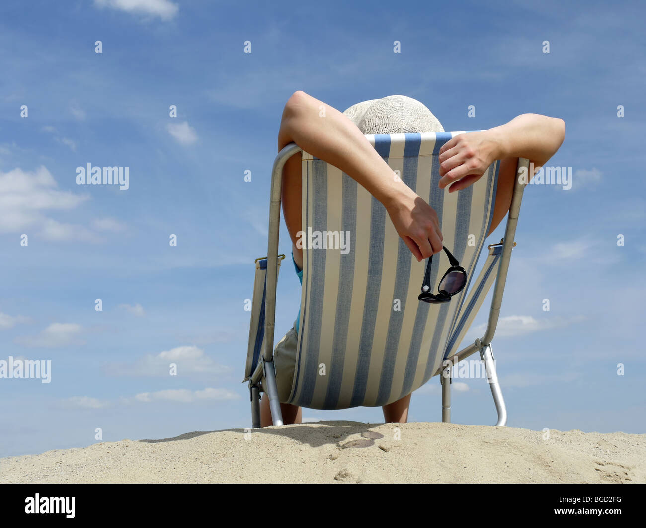 Femme en train de bronzer sur une chaise longue sur la plage tourné contre le ciel bleu Banque D'Images