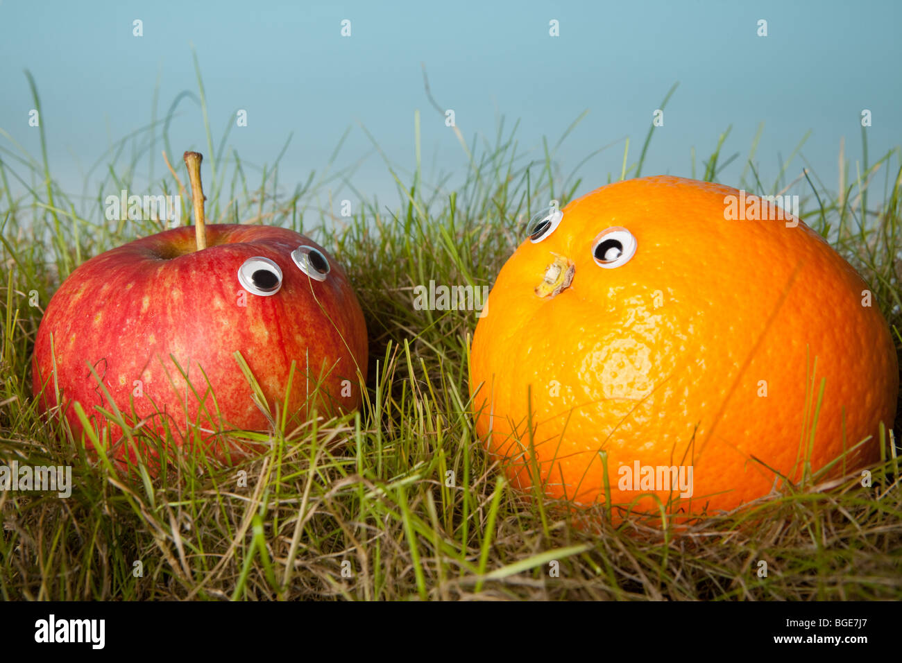 Apple et d'orange avec Smiley yeux in Green grass Banque D'Images