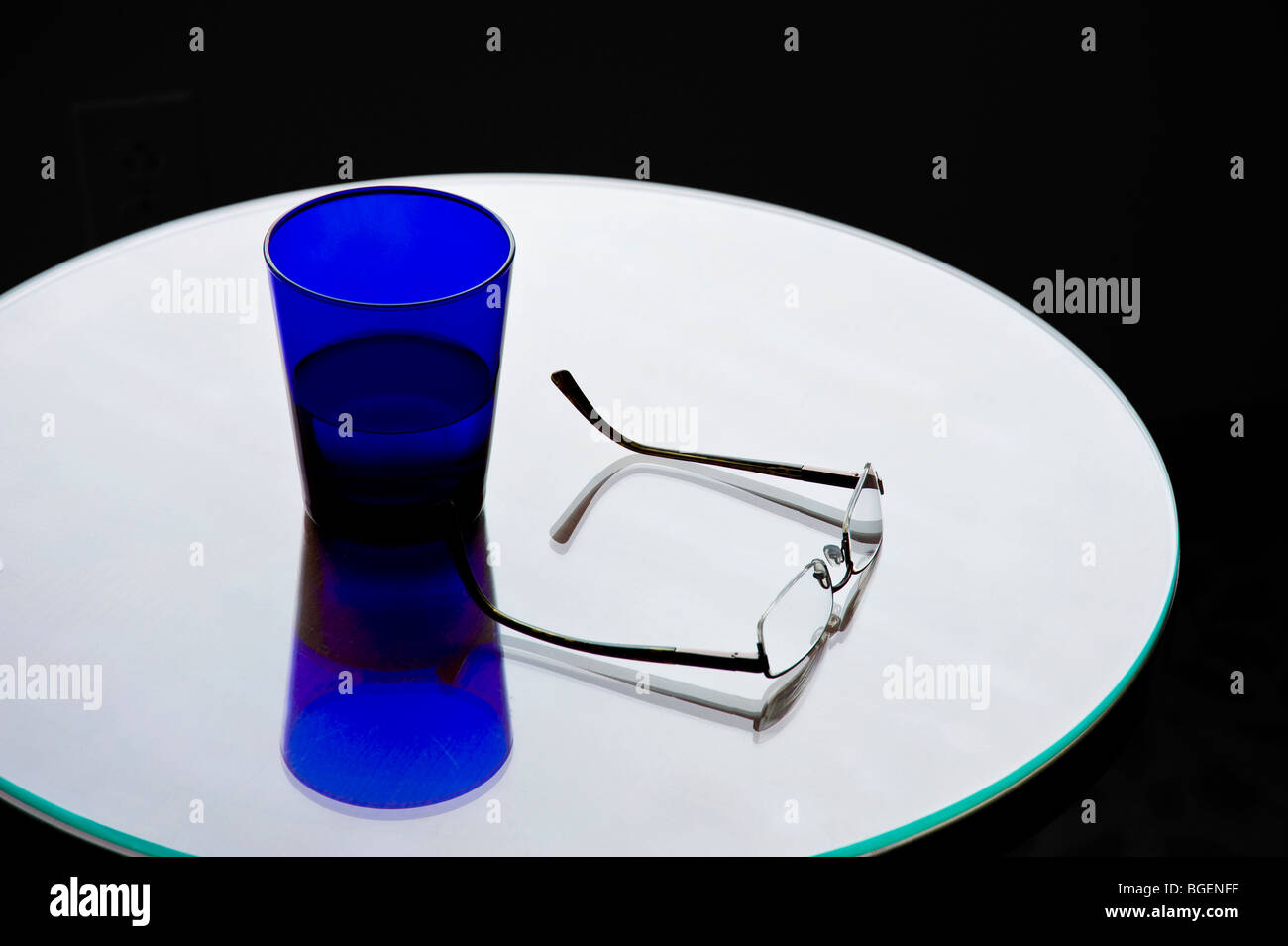 Verre de l'eau bleu et les lunettes sur la Table ronde de réflexion brillant Banque D'Images