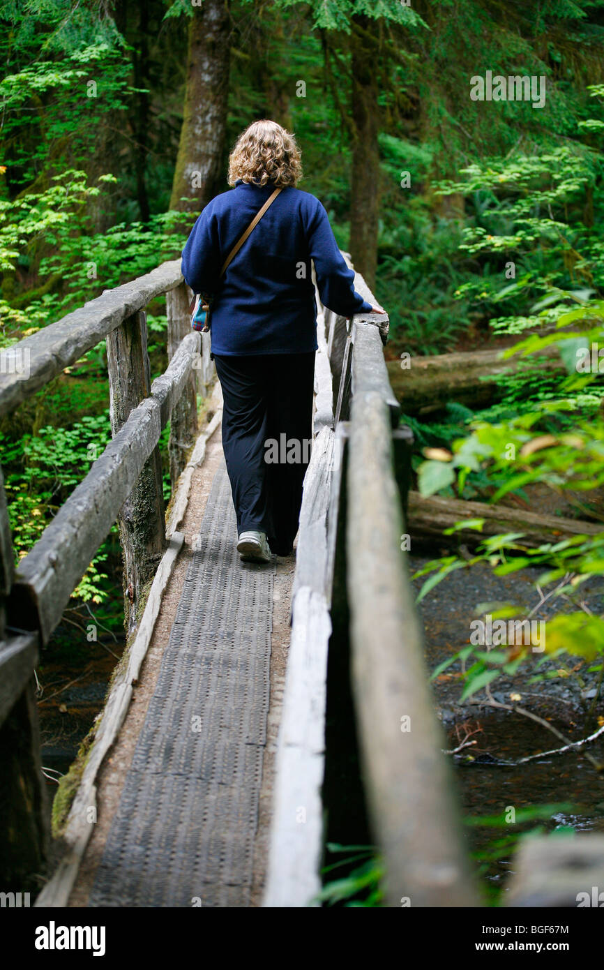 Femme marche sur un pont sur la piste vers Marymere Falls, sur la péninsule Olympique, Olympic National Park, Washington State. Banque D'Images