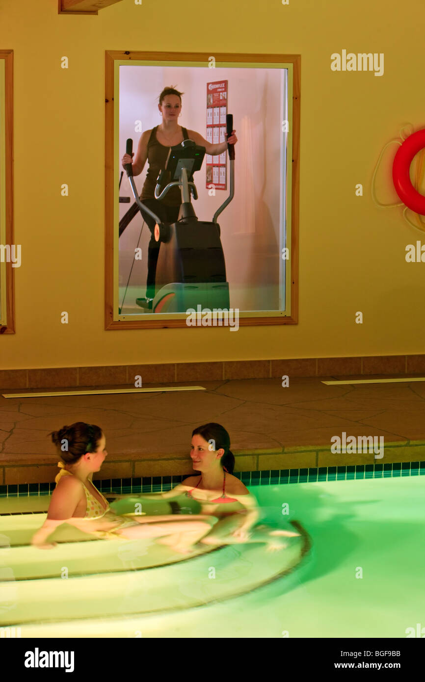 Deux femmes se baigner dans la piscine et d'une femme travaillant sur un entraîneur elliptique dans le centre de remise en forme du Black Bear Resort & Banque D'Images