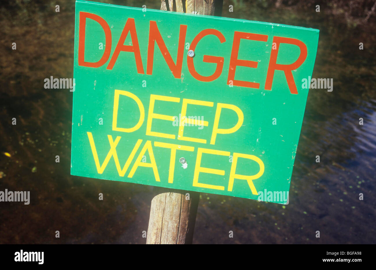 Panneau en bois sur perche avec de l'eau et de la boue derrière peint en vert avec lettrage rouge et jaune de l'eau profond Danger Banque D'Images Panneau en bois sur perche avec de l'eau et de la boue derrière peint en vert avec lettrage rouge et jaune de l'eau profond Danger Banque D'Images