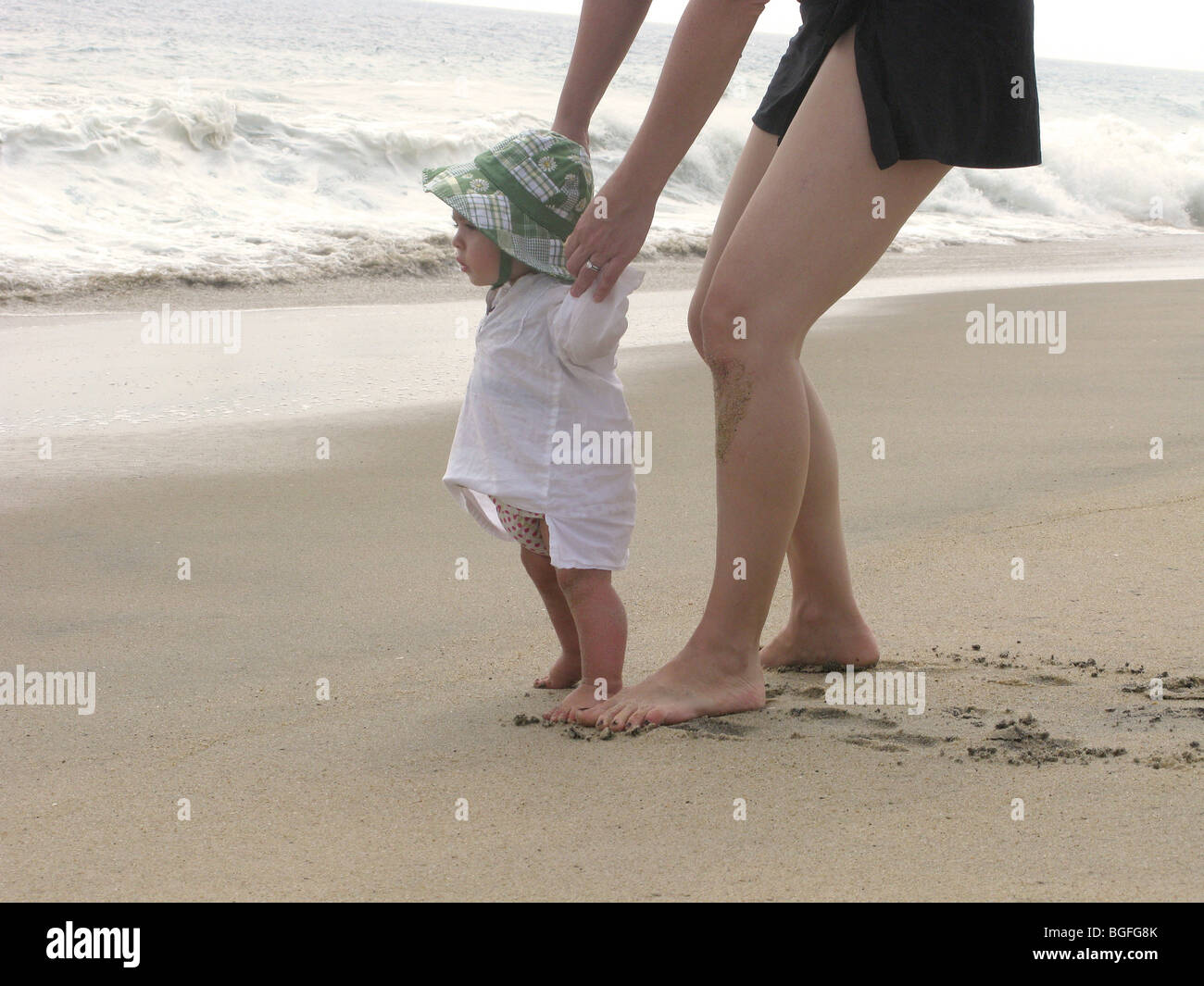 Une mère tenant les mains d'une petite fille debout au bord de l'eau Banque D'Images