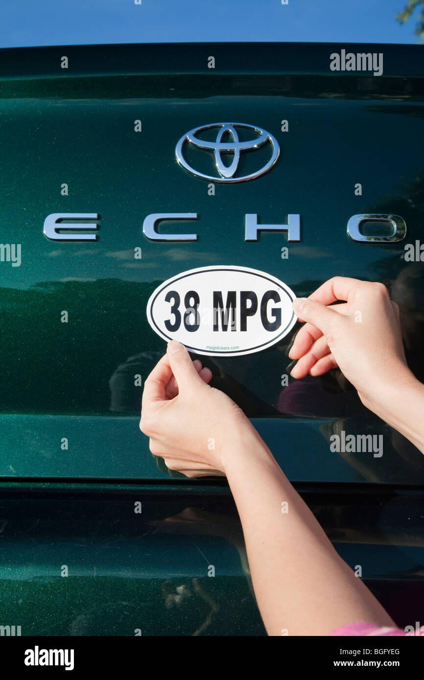 Près d'une femme en joignant une 38 miles par gallon de carburant autocollant de pare-choc installé sur Toyota Echo voiture. La Californie, USA Banque D'Images Près d'une femme en joignant une 38 miles par gallon de carburant autocollant de pare-choc installé sur Toyota Echo voiture. La Californie, USA Banque D'Images