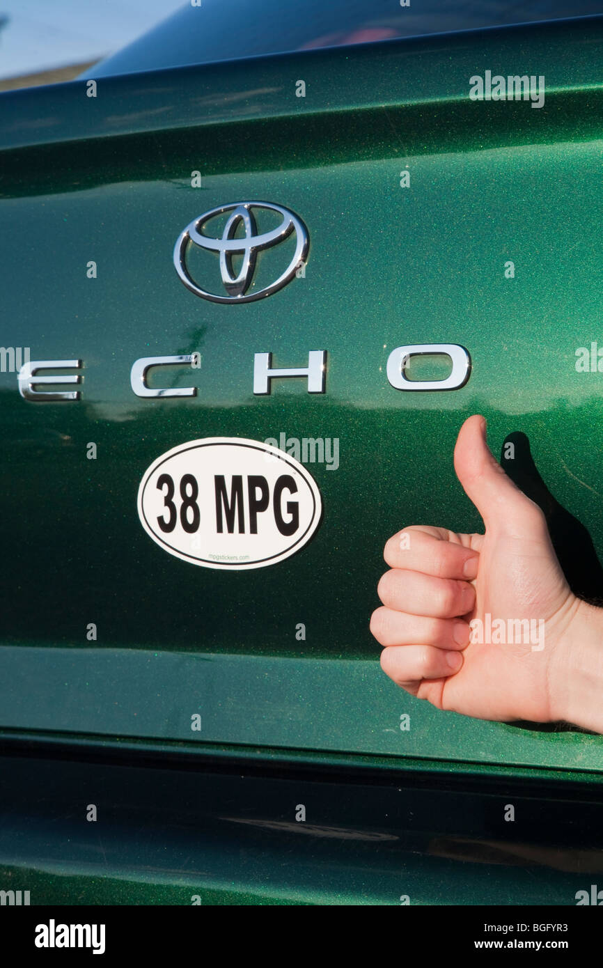 Close up of person holding Thumbs up près de 38 miles par gallon de carburant autocollant sur Toyota Echo vert voiture. Banque D'Images