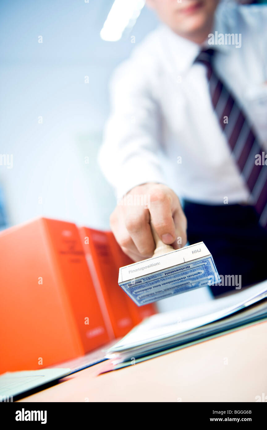 Homme tenant un timbre au-dessus d'une pile de papiers, sur l'incliné Banque D'Images