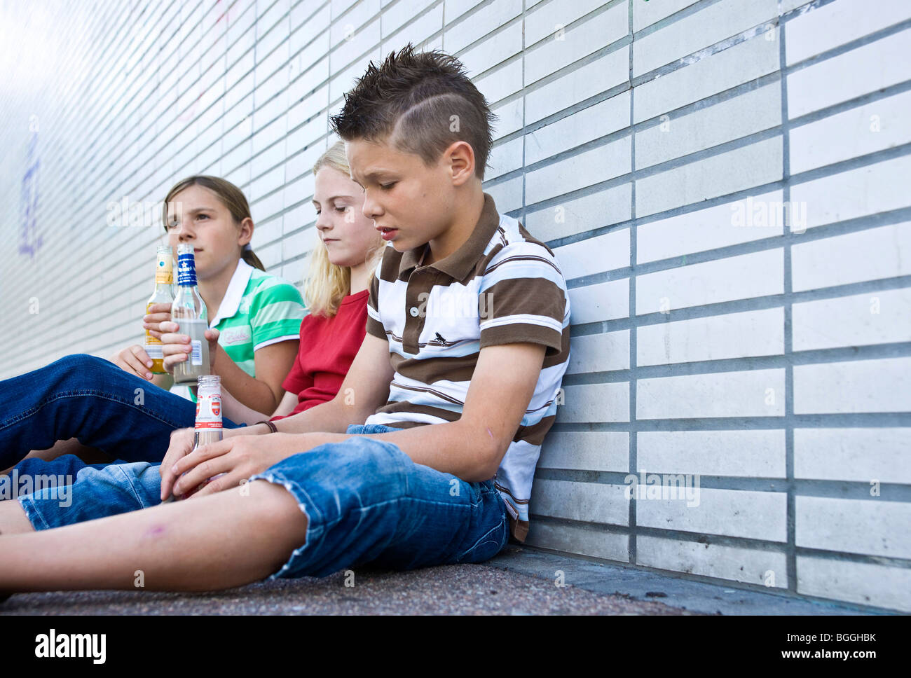 Trois enfants assis sur le sol et la tenue de bouteilles d'alcool, low angle view Banque D'Images