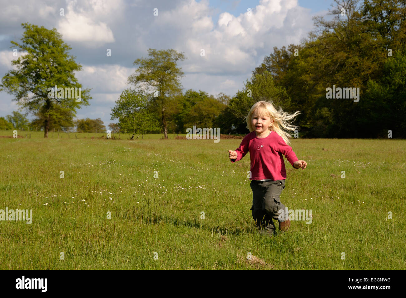 Stock photo d'un enfant de 3 ans aux cheveux blonds fille courir dans un champ. Banque D'Images