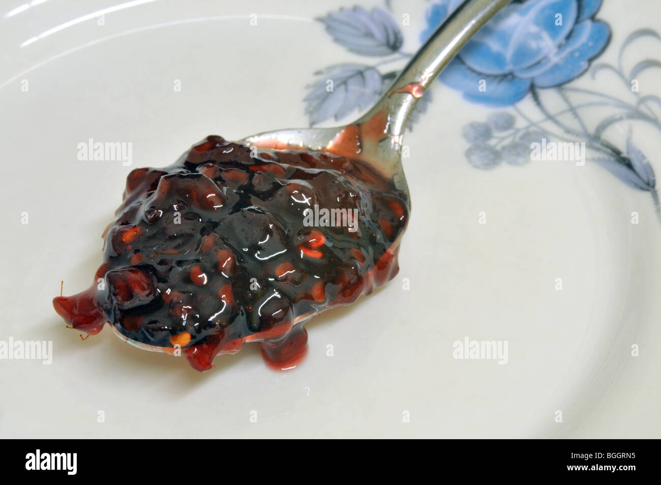 Une cuillerée de confiture de framboises en appui sur un côté floral chine plaque. Banque D'Images