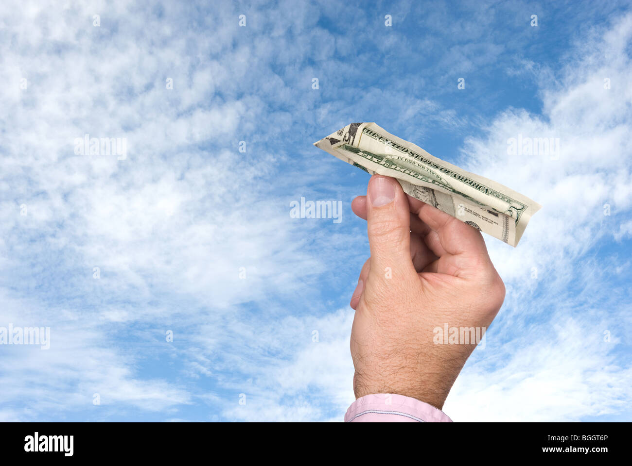 Un homme jette un avion en papier fait d'un billet de cinq dollars dans un ciel bleu avec des nuages blancs, gonflées. Banque D'Images