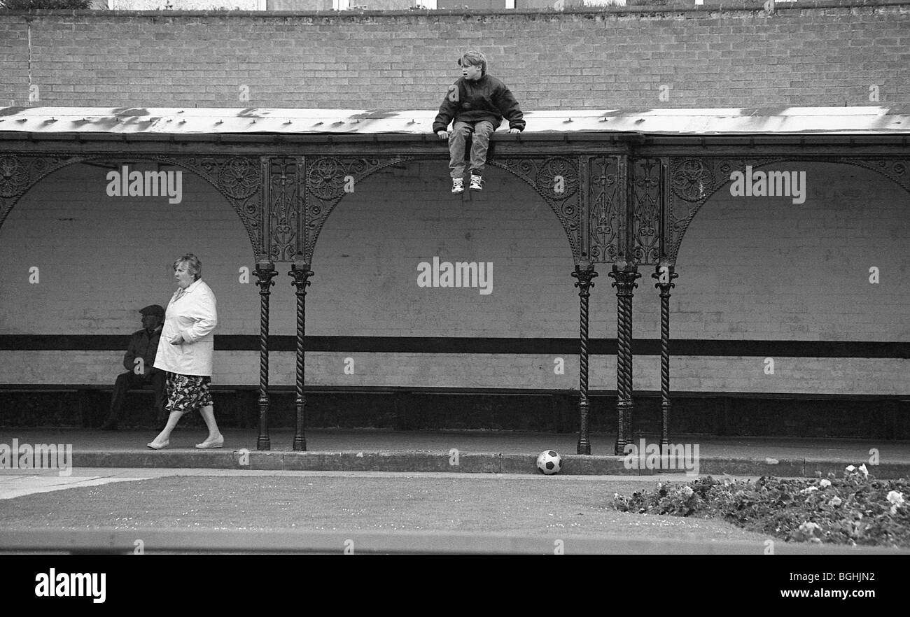 Garçon assis sur le toit que personne marche par. Banque D'Images