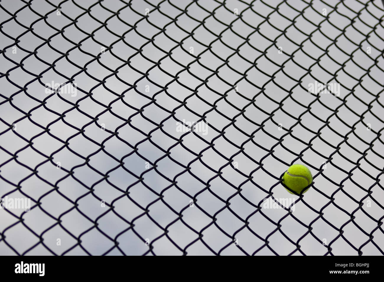 Une seule balle de tennis coincé dans la clôture à un court de tennis, avec un ciel couvert à l'arrière. Banque D'Images