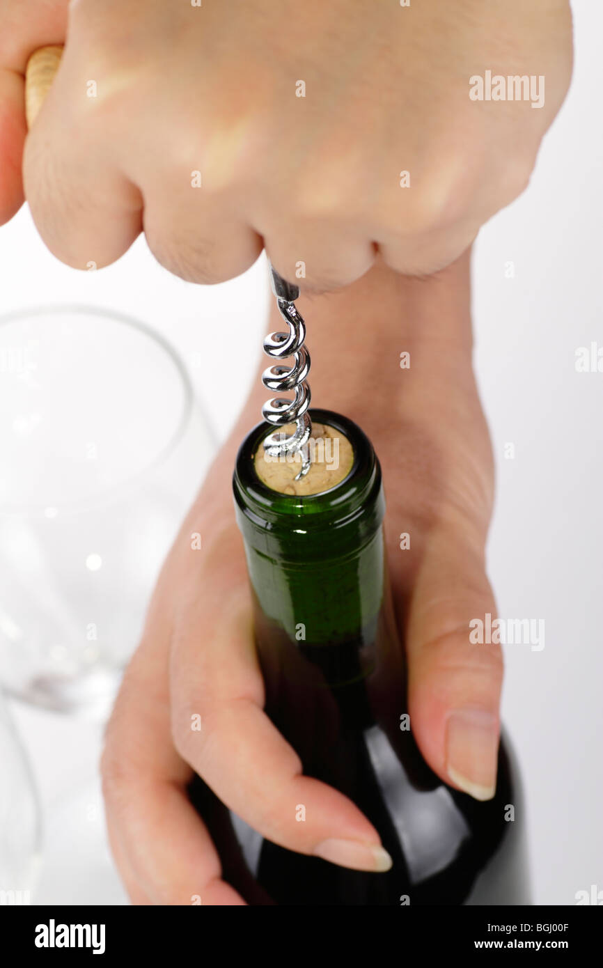 Les mains d'une femme d'ouvrir une bouteille de vin avec un tire-bouchon. Un verre de vin vide est dans l'arrière-plan Banque D'Images