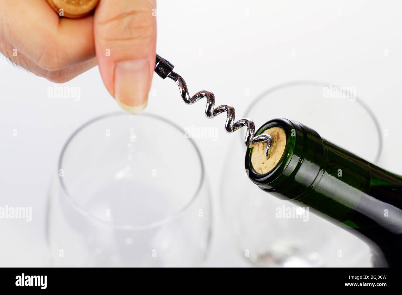 A woman's hand l'ouverture d'une bouteille de vin avec un tire-bouchon. Deux verres à vin sont vides à l'arrière-plan Banque D'Images