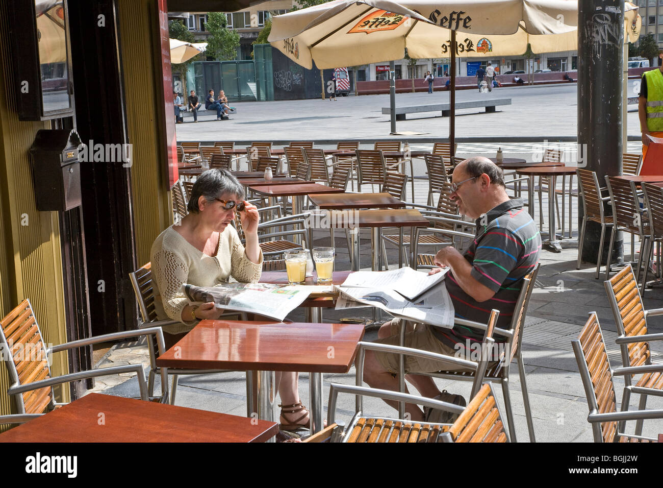 Couple d'âge moyen assis café à l'extérieur de lire les journaux Banque D'Images