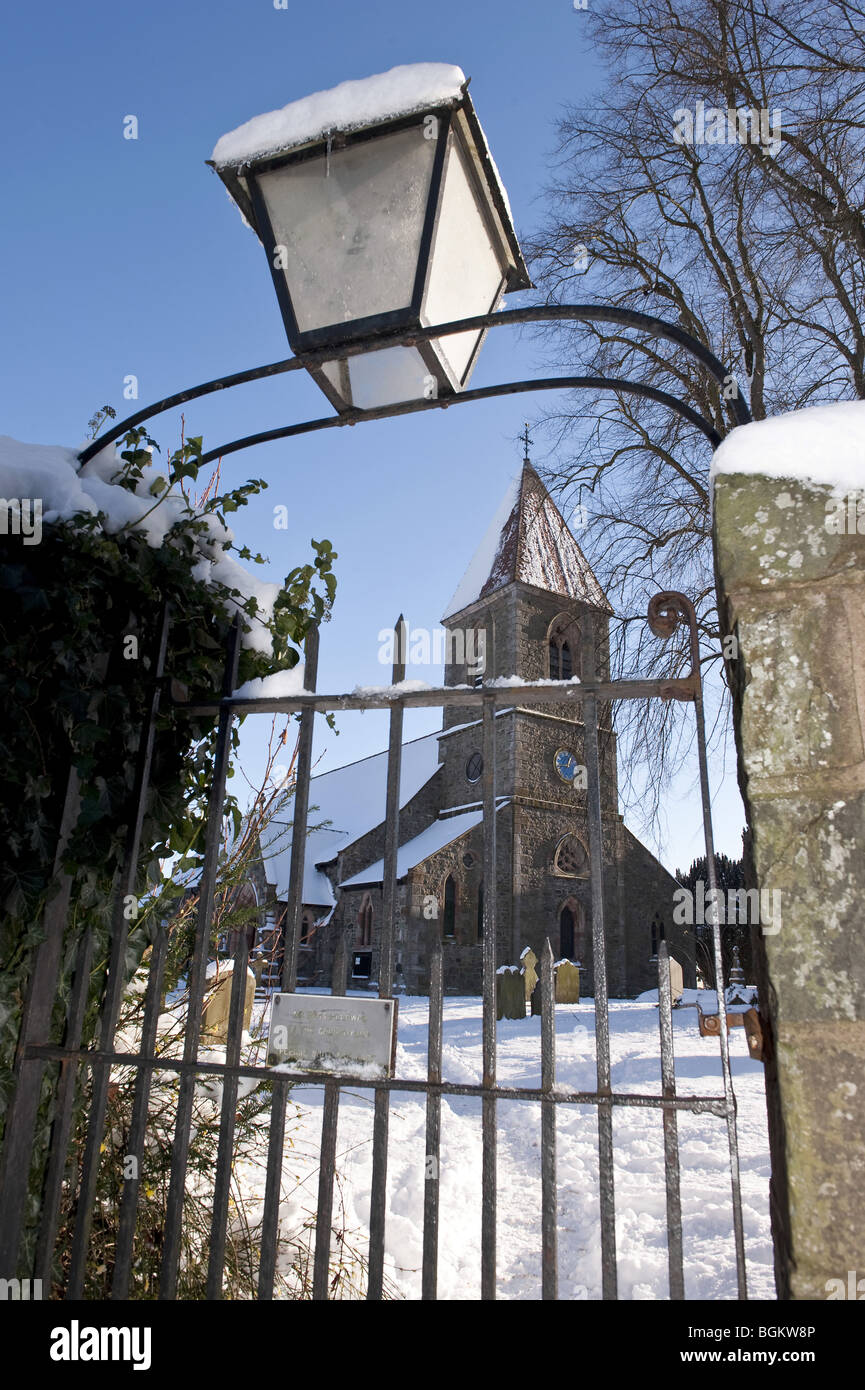 Vue à travers une grille de fer avec lanterne pour un couvert de neige village aux murs de pierre et église cimetière memorial against a blue sky Banque D'Images