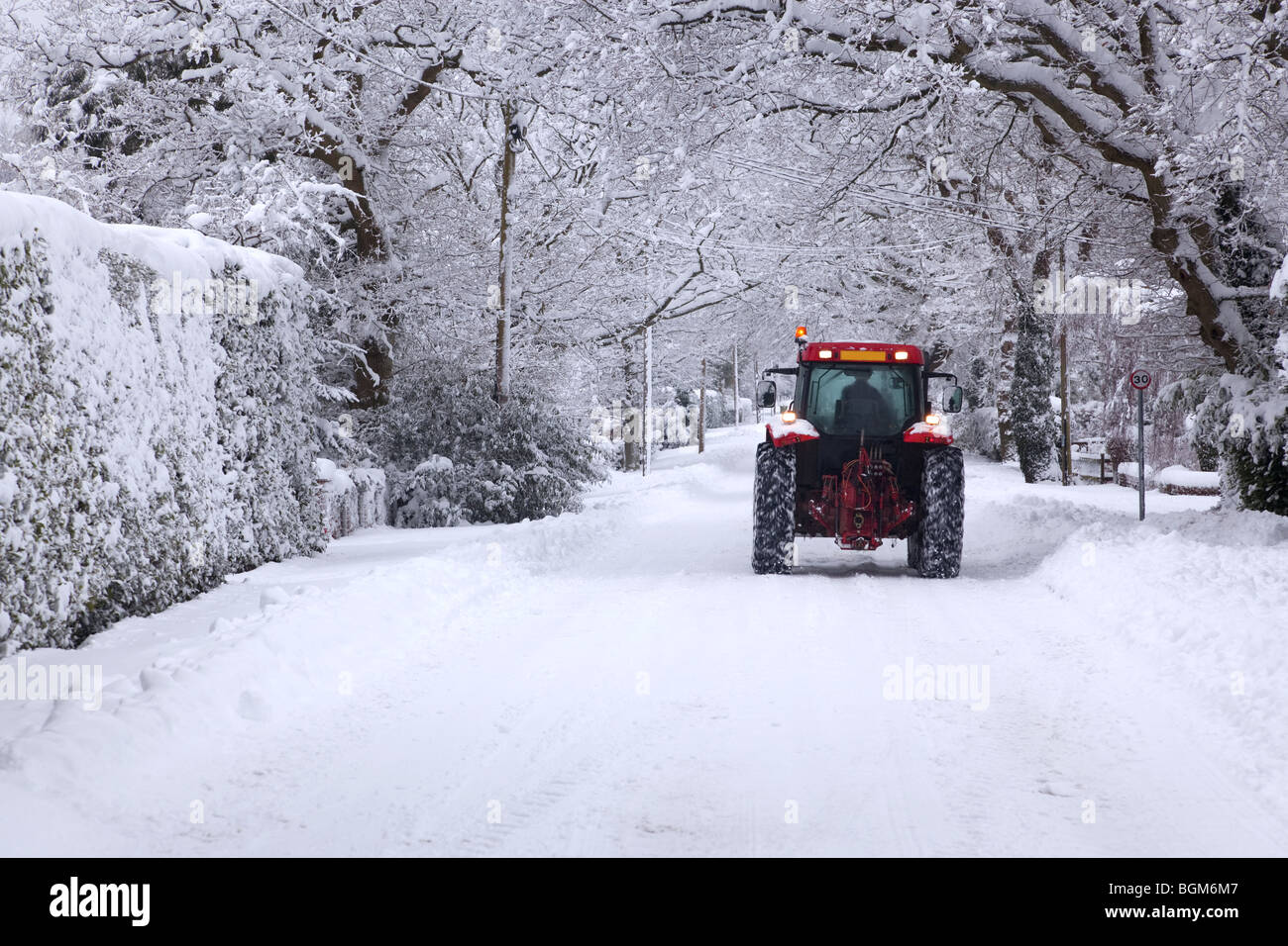 Un tracteur rouge descendre une route couverte de neige UK au cours de l'hiver hiver neige en janvier 2010 Banque D'Images