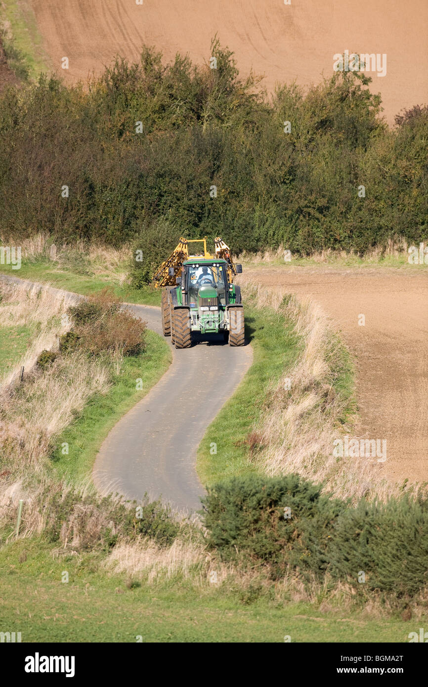 Le tracteur et le pulvérisateur voyageant sur un étroit chemin de campagne Banque D'Images