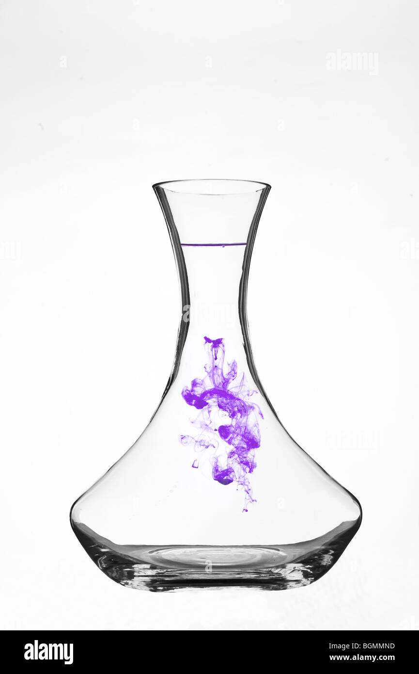 Colorant coloré se dispersant dans l'eau à l'intérieur d'une carafe en verre transparent sur fond blanc. Banque D'Images