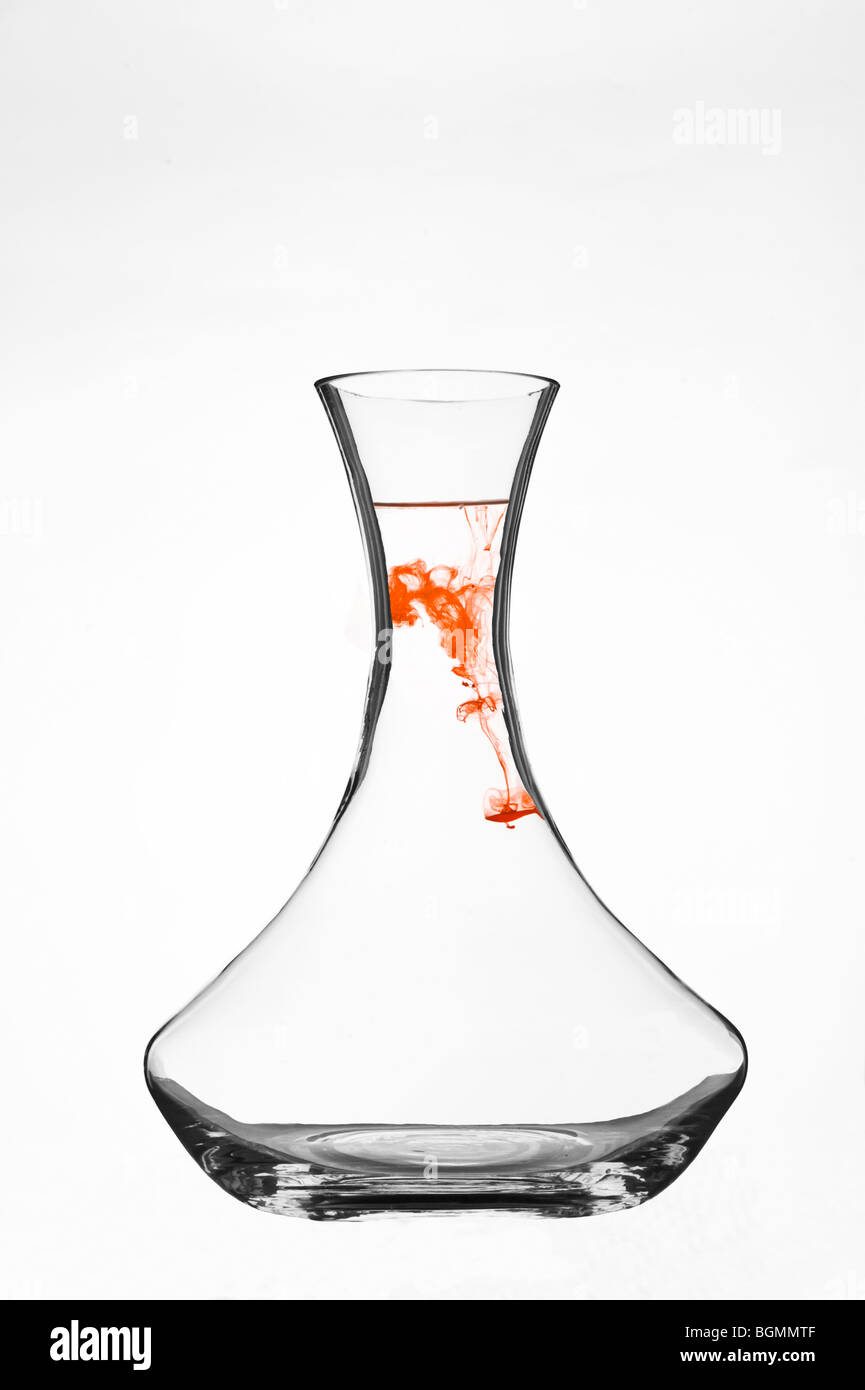 Colorant coloré se dispersant dans l'eau à l'intérieur d'une carafe en verre transparent sur fond blanc. Banque D'Images