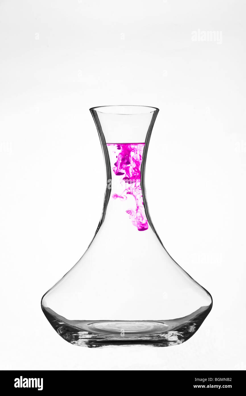 Colorant coloré se dispersant dans l'eau à l'intérieur d'une carafe en verre transparent sur fond blanc. Banque D'Images