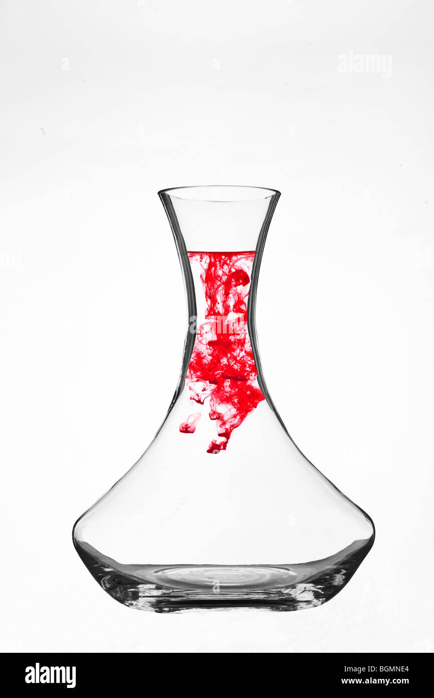 Colorant coloré se dispersant dans l'eau à l'intérieur d'une carafe en verre transparent sur fond blanc. Banque D'Images