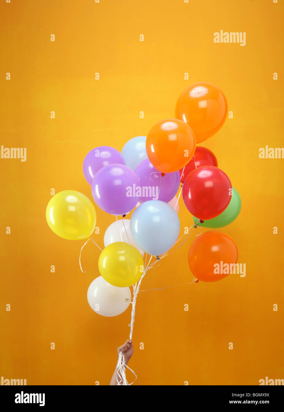 Ballons colorés dans un groupe organisé par une main avec fond orange Banque D'Images